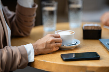 Businesswoman drinking cappuccino at cafe with laptop and smartphone