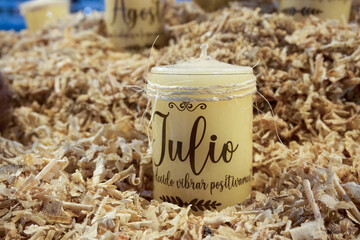 A candle with the name Julio written on it is sitting on a pile of wood shavings. The candle is yellow. Mexico, Puebla, Chignahuapan, decorative Christmas balls with colorful designs