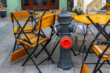 Blocked fire hydrant by folding chairs and restaurant tables, safety hazard, urban infrastructure issue in public outdoor space