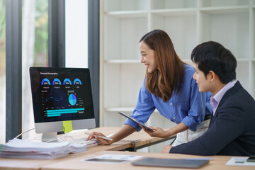 Two asian business colleagues analyzing financial charts on a computer screen, discussing data and reports, collaborating on a project in a modern office