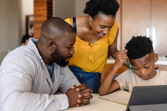 Parents helping son with homework using tablet at home, focusing on learning