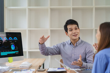 Young professional explaining marketing data on computer screen to female colleague during a meeting in a modern office