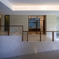 Contemporary interior with smooth tile walls, wooden and glass railings, and multi-level stairs and ramps. Soft lighting enhances the serene, modern atmosphere.