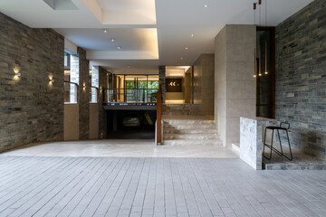 Wide-angle lobby with light tile floors, marble stairs, and striking stacked stone walls. A car is visible in the parking area outside.