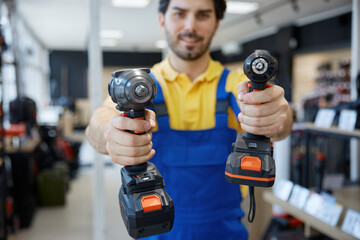 A man worker is holding impact and power drills in his hands in a store