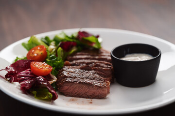 ribeye steak with garlic sauce and fresh salad on white plate on walnut table