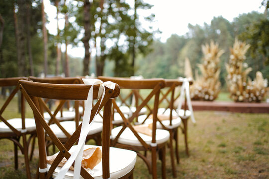 Rows of chairs with white bows prepared for wedding ceremony in forest location.
