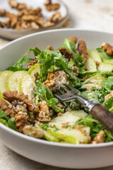 Salad with Pear, Arugula, cheese and walnuts with fork close up. Delicious Fresh Salad on light textured background