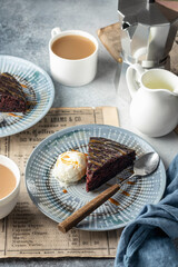 A piece of chocolate brownie cake on blue plate served with a scoop of ice cream and caramel topping with coffee