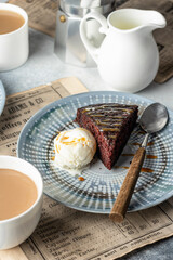 A piece of chocolate brownie cake on blue plate served with a scoop of ice cream and caramel topping with coffee