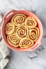 Raw cinnabon buns in a ceramic baking dish on white marble background top view. Making cinnamon rolls process. Cinnabon preparation