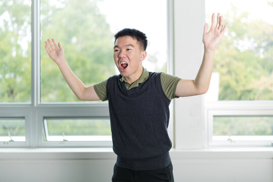 Young man mid performance with hands raised, conveying intense emotion and expression as if acting or presenting in drama class. - Powered by Adobe