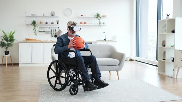 Senior man sitting in wheelchair indoors wears VR headset holding basketball, enjoying technology. Interior setting includes sofa, shelves. Emphasizes virtual reality, accessibility