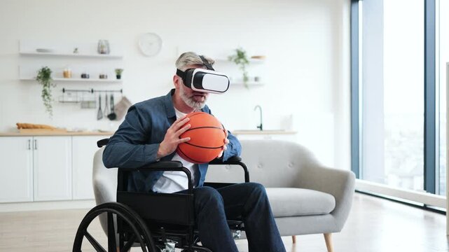Senior man sitting in wheelchair indoors wears VR headset holding basketball, enjoying technology. Interior setting includes sofa, shelves. Emphasizes virtual reality, accessibility