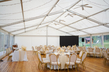 Wedding marquee with round tables, chairs and decor in light tones.