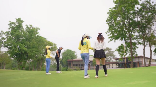 Asian male and female golfers walk across lush green fairway with caddy. 