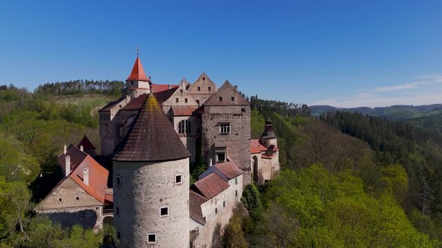Dramatic aerial drone flyby of the fortified Pernstein Castle, highlighting its Renaissance and Gothic architecture perched atop a massive rock formation overlooking Nedvedice, Czechia.