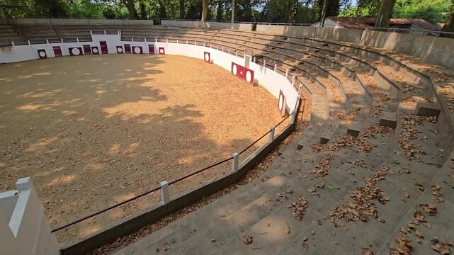 Deserted bullring captured from above showing empty rows of concrete seats and central sand arena where fights took place.
