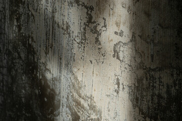 An abstract texture background of an old, peeling concrete wall with a diagonal sunbeam.