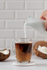 Coconut milk pouring into coffee glass with coconut shells on white background. Plant milk