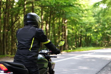 Young man in helmet driving modern motorcycle outdoors, back view. Space for text