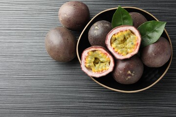 Fresh passion fruits with green leaves on black wooden table, above view. Space for text