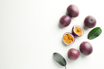 Fresh passion fruits with green leaves on white table, flat lay. Space for text