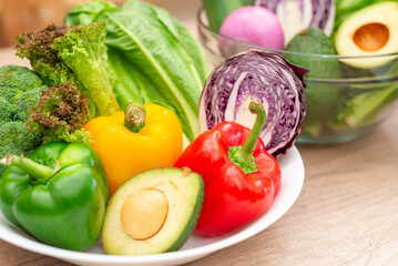 Assortment of vibrant fresh raw vegetables including bell peppers, avocado, broccoli, and lettuce on a white plate, symbolizing healthy eating for a balanced diet.