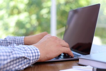 Man working on laptop at wooden table indoors, closeup