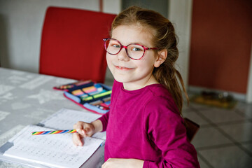 Little school girl learning at home. Elementary class student chid doing maths homework, writing...