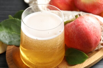 Fresh cider in glass, apples and green leaves on table, closeup