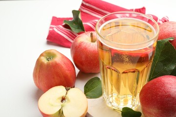 Fresh cider in glass and apples on white table, closeup