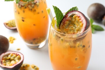 Tasty passion fruit drink with mint in glasses and fresh fruits on light table, closeup