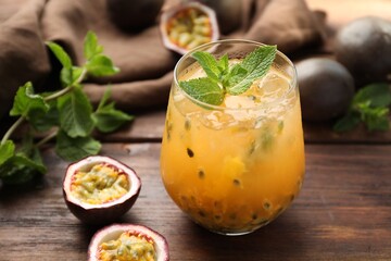 Tasty passion fruit drink with mint in glass and fresh fruits on wooden table, closeup