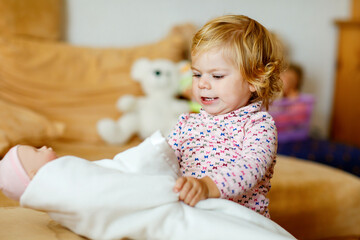 Fototapeta premium Adorable cute little toddler girl playing with doll. Happy healthy baby child having fun with role game, playing mother at home or nursery. Active daughter with toy.