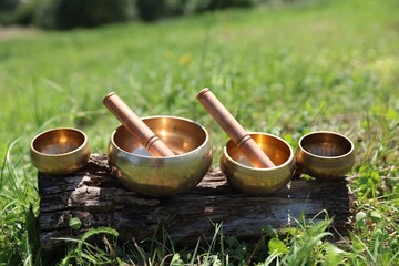 Tibetan singing bowls with mallets on piece of wood outdoors