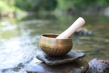 Tibetan singing bowl with mallet on stone near river