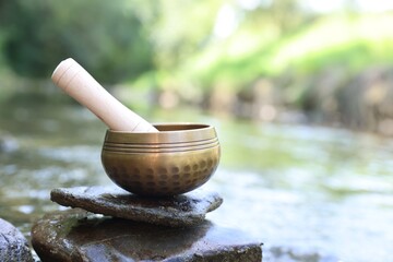 Tibetan singing bowl with mallet on stone near river, closeup