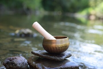 Tibetan singing bowl with mallet on stone near river
