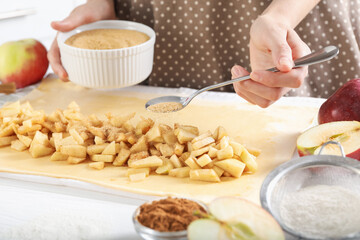 Woman making delicious apple strudel at white table in kitchen, closeup