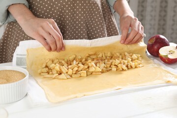 Woman making delicious apple strudel at white wooden table in kitchen, closeup