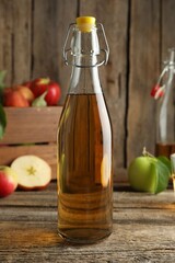 Delicious cider in glass bottle and apples on wooden table, closeup