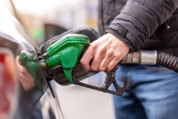 Obraz premium A close-up of the hand holding green fuel gun, filling gas into car tank at station
