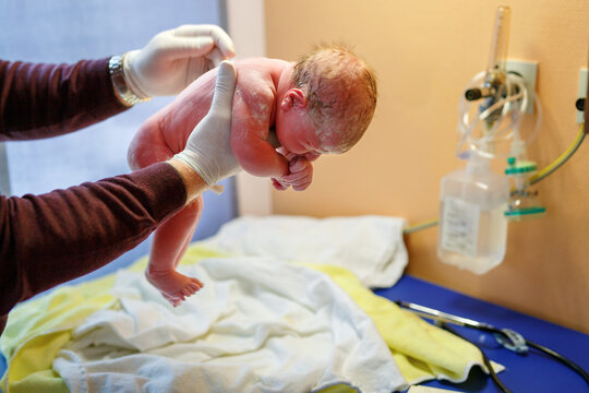 Newborn child seconds and minutes after birth. Doctor hands with new born baby. Medical check up of health and reflexes of child. New life, beginning, healthcare