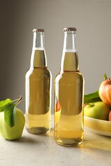 Delicious cider in glass bottles and apples on gray table against light background