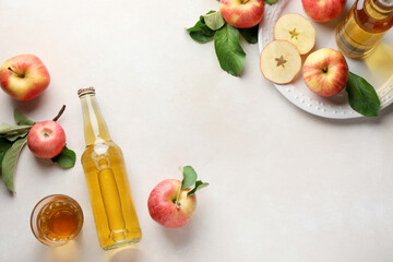 Delicious cider in bottles, glass and apples with green leaves on beige table, flat lay. Space for text