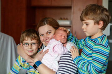 Mother holding newborn baby girl in hospital bed, with two sons sitting beside her. Real life, real people moment of family love, siblings bonding, and joy of welcoming a new child.