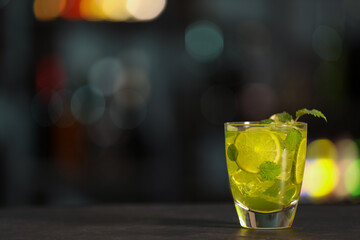 Glass of alcoholic cocktail with lime slices on table against blurred background. Space for text