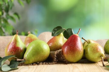 Fresh ripe pears on wooden table and green leaves outdoors, closeup