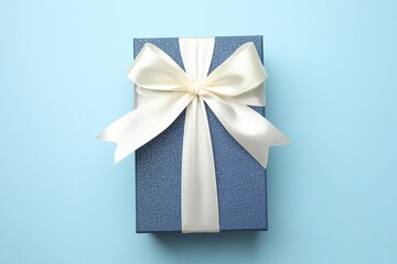 Gift box with beautiful bow on light blue background, top view